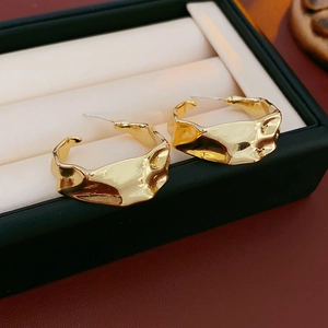 Macro shot of gold C-shaped earrings with wrinkled lava texture on a jewelry box edge