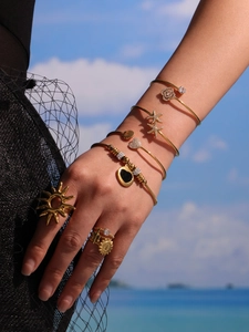 Détail de bracelets océan dorés et bagues cœur portés lors de vacances à la plage