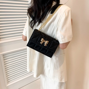Schwarze gesteppte Schultertasche mit goldener Schleife und Kette am Modell