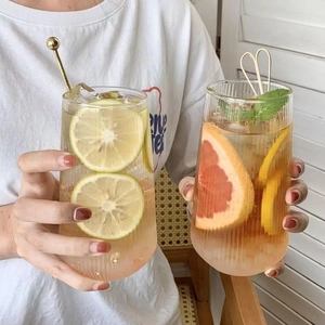 Close-up of vertical striped glass cups with fresh lemon and mint drinks in hand