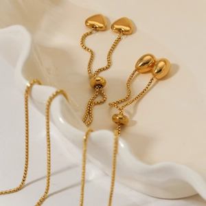 Elegant gold heart pendant earrings with box chain and adjustable sliding beads in a ceramic dish