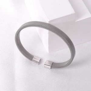 Detail view of a silver woven mesh bangle bracelet with rectangular ends on white fabric