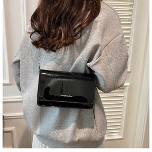 Chic black patent leather crossbody square bag with metal chain strap on grey sweater