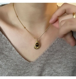 Primo piano di un ciondolo a goccia dorato con occhio di tigre marrone su maglia grigia