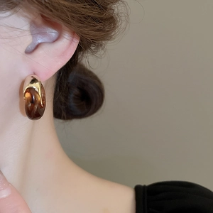 Close-up of amber resin and gold metal C-shape hoop earring worn by a model