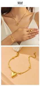 Polished gold heart jewelry set featuring necklace and bracelet on warm beige background