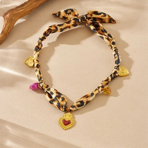 Detail of leopard print fabric choker with gold heart pendant on a sandy surface