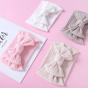Flat lay of four waffle knit baby headbands with bows in pink, white, beige, and taupe