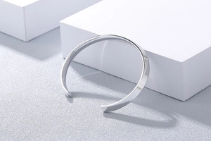 Close-up of minimalist silver C-shaped open bangle on white geometric block