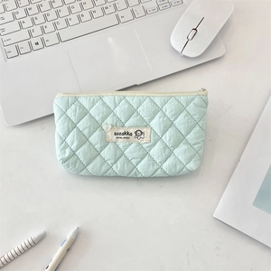 Close-up of mint green quilted makeup bag with dog label on a minimalist white desk