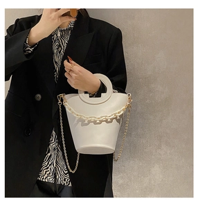 White bucket bag featuring round handles and thick acrylic chain shown on model