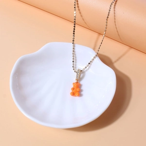 Detail view of orange resin bear pendant on a gold chain with zircon inlay stones