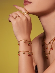 Détail d'une parure de bijoux cerise dorée avec colliers et bagues en perles sur un modèle