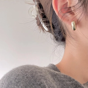 Close-up of minimalist gold oval stud earrings worn by a model in a modern style