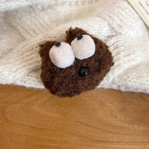Close-up of a cute brown plush cartoon brooch with big eyes on a white knit sweater