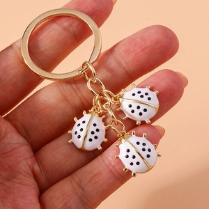 Cute white ladybug keychain pendant with gold metal hardware held in hand