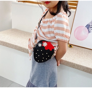 Detail of a black strawberry shaped crossbody bag with floral accents on a child model