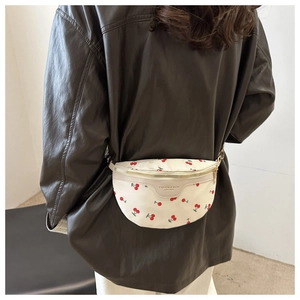 Detail of beige canvas waist bag featuring red cherry prints and adjustable strap worn on back