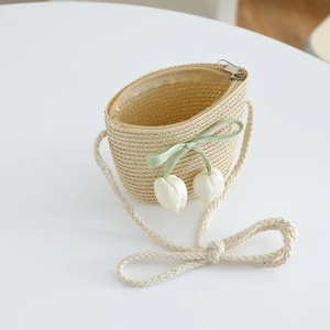 Detail of a beige straw crossbody bag featuring green satin bows and white tulip charms