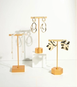 Three elegant earring styles displayed on gold T-bar stands with marble and pearl accents