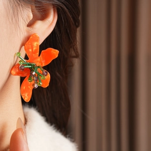 Close-up of model wearing orange glass flower earrings with beaded crystal detail