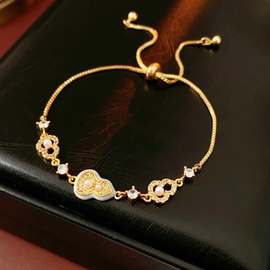 Detailed shot of a gold-plated bracelet with pearls and heart charms on a black leather box