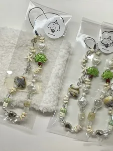 Detail of beaded phone charms with shell and palm tree pendants in clear packaging