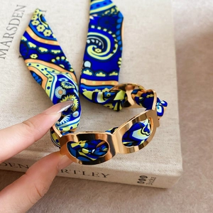 Detail view of gold metal open bangle wrapped with a blue paisley pattern silk scarf wrap