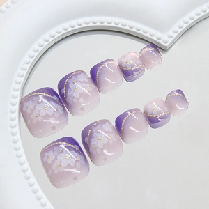 Glittery purple gradient press-on toenails with white floral patterns and gold accents