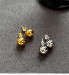Detailed view of polished gold and silver spherical stud earrings with silicone backings
