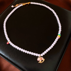 Détail du collier de perles avec pendentif cheval à bascule en émail rose sur fond noir