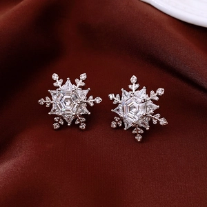 Macro detail of silver snowflake stud earrings featuring sparkling zircon on velvet background