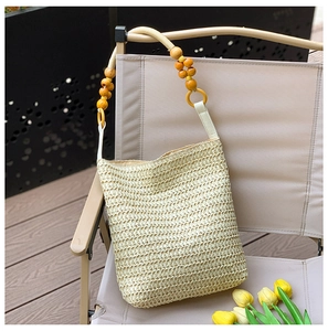 Detail of beige straw tote bag featuring decorative wooden bead shoulder strap in outdoor light