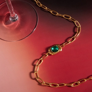 Close-up of gold paperclip chain necklace featuring a square green gemstone centerpiece