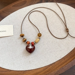 Détail macro du pendentif coeur rouge avec emblème orb argenté et perles en bois