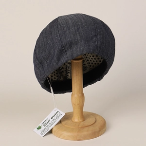 Detail of dark blue hemp denim beret featuring a branded tag on a wooden display stand