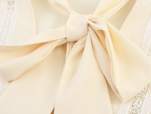 Detail of elegant beige linen shirt with lace trim and large decorative bow tie