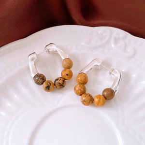 Detail of vintage C-shaped silver earrings with brown spotted stone beads on white ceramic