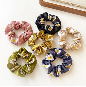 Detailed flat lay of six assorted daisy floral satin scrunchies on white background