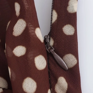Deep brown polka dot chiffon dress featuring a concealed zipper and ruffled hem details