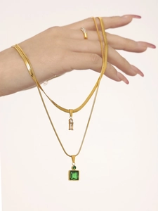 Detail of layered gold snake chain and thin necklace with green square gemstone pendant