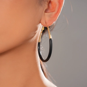 Detailed view of large black and gold oval hoop earring worn by a model in soft lighting