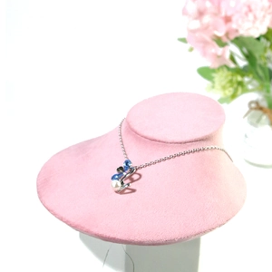 Detailed view of silver necklace with blue crystal and pearl on pink velvet display