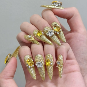Detailed close-up of golden stiletto press-on nails with luxury butterfly and rhinestone charms