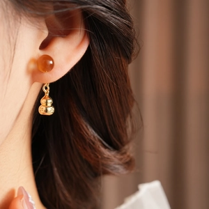 Close-up of a model wearing a gold gourd drop earring with a translucent orange bead