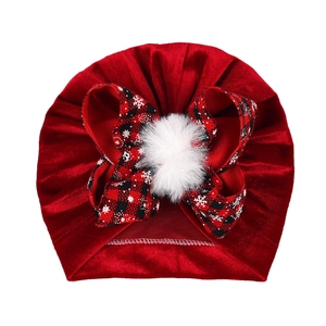 Red velvet baby turban hat with a red and black plaid bow and a white fluffy pompom