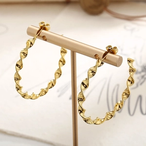 Elegant gold twisted wave earrings on a metal display stand with warm vintage background