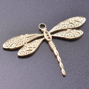 Macro shot of 18k gold plated dragonfly pendant with intricate embossed wing patterns