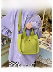Detail of light green canvas tote bag with front pocket shown on shoulder