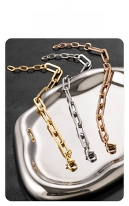 Three paperclip link bracelets in gold, silver, and rose gold on a metallic tray